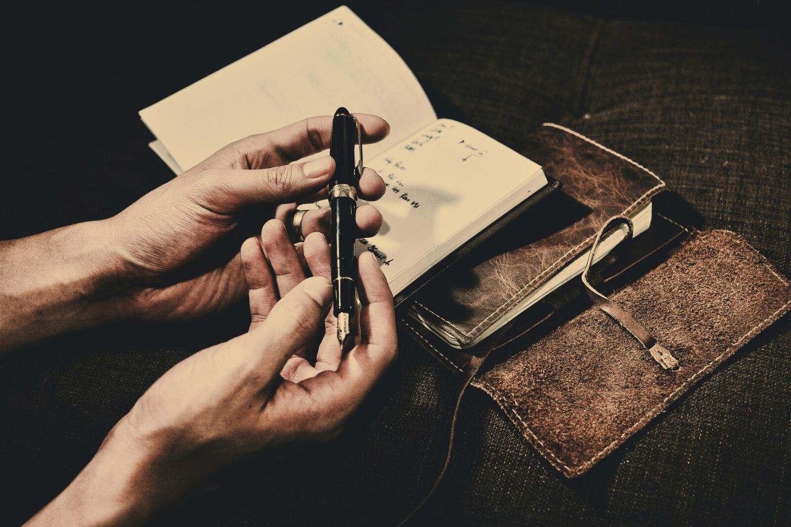 Hands with a fountain pen and an open leather-bound notebook