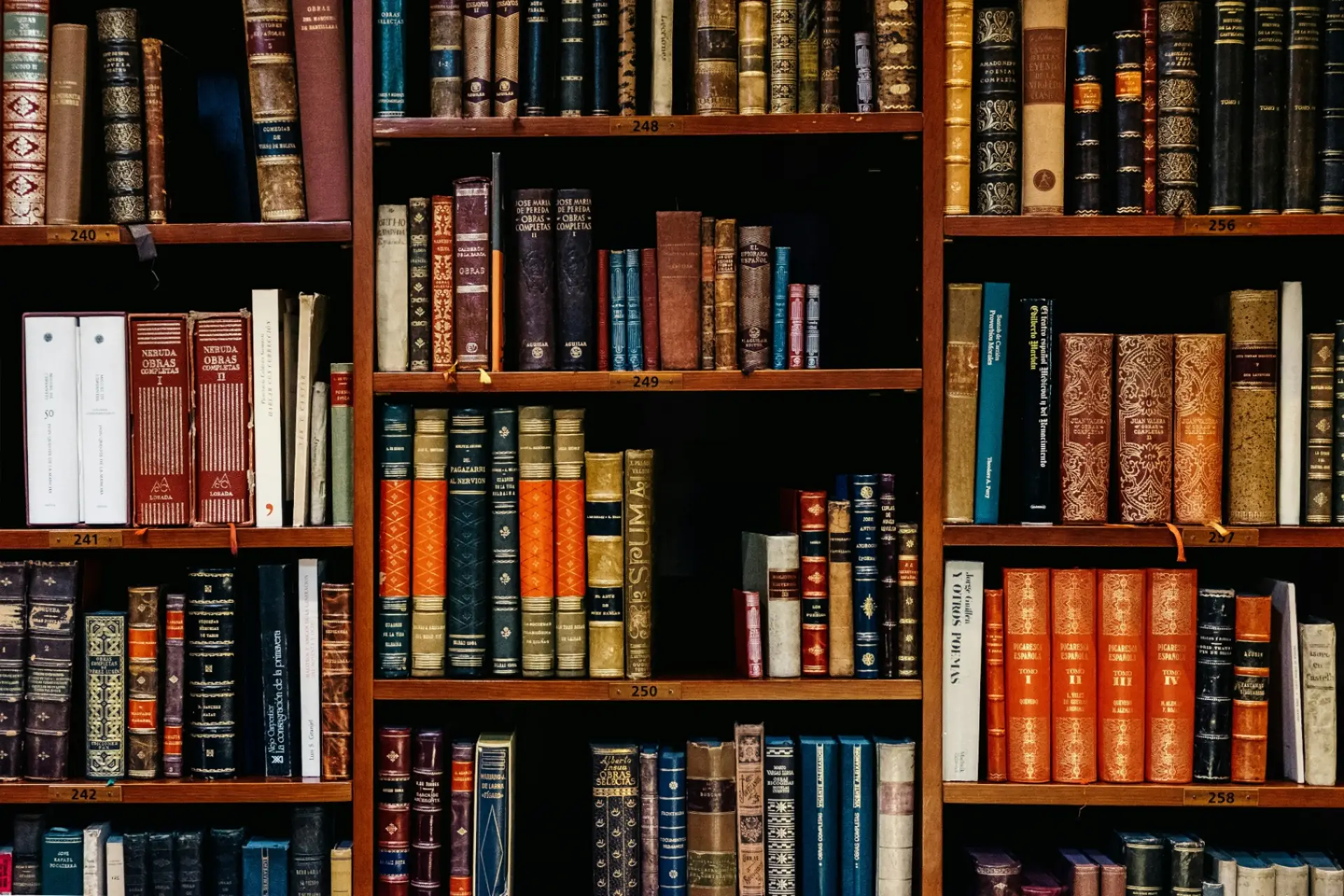 Wall of antique leather-bound books on wooden library shelves